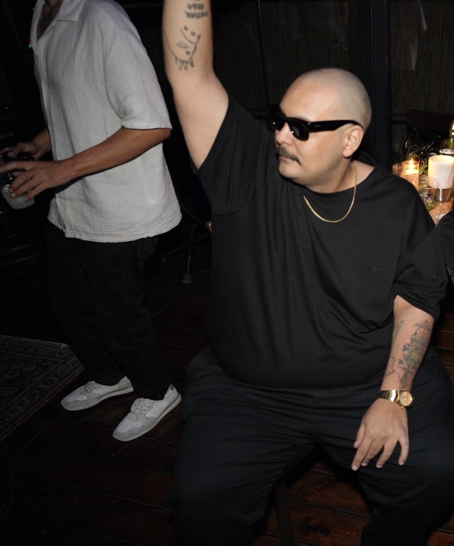 Deniz Agah wearing black sunglasses and raising his arm in a nightlife setting