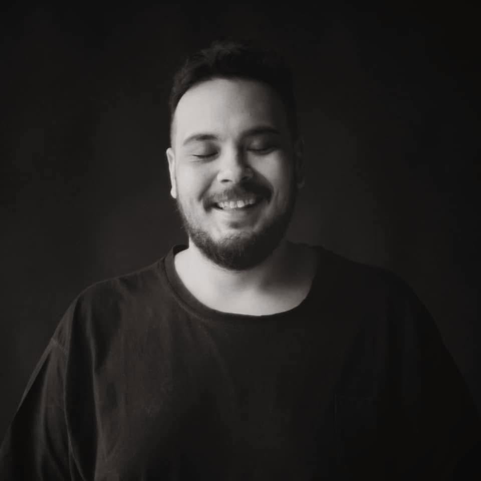 Black-and-white portrait of Deniz Agah smiling with his eyes closed